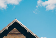 Close Up Of Triangular Roof Of Modern Log House Against Bright Blue Sky With White Clouds. Copy Space