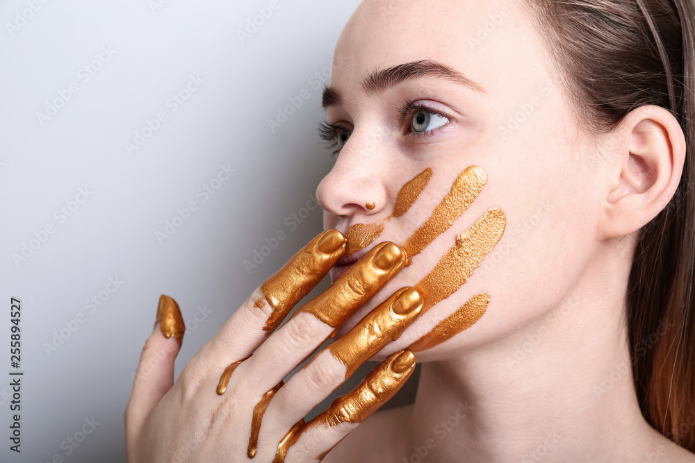 Woman with golden paint on her face against light background