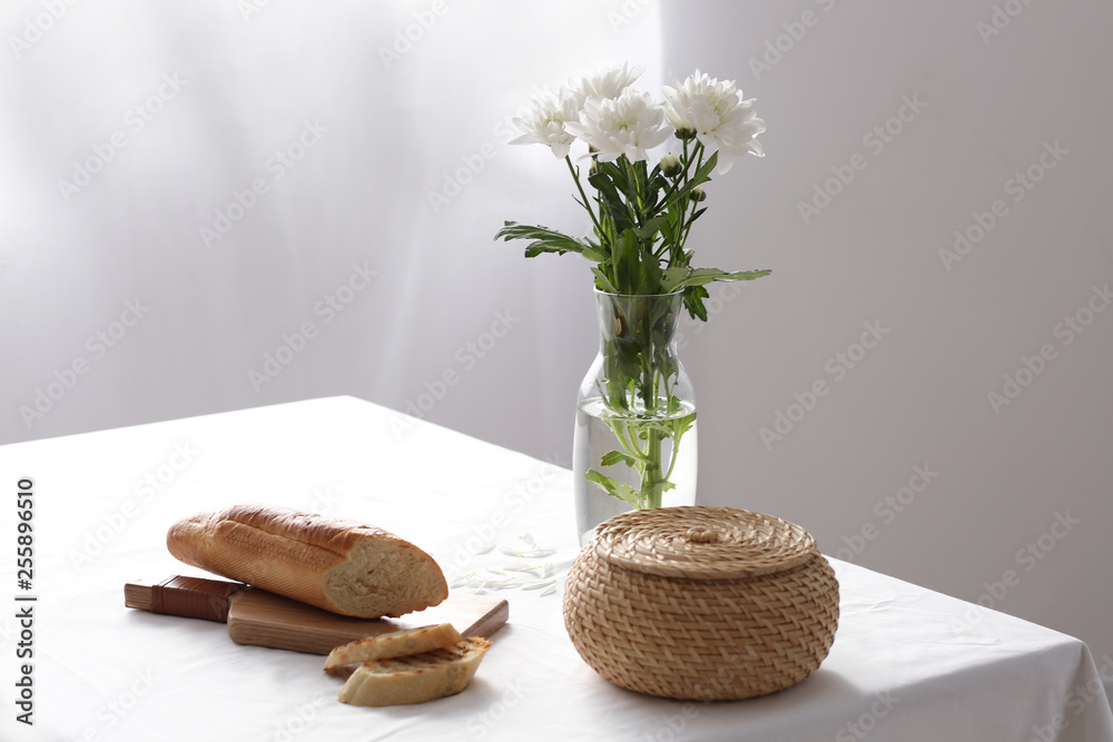 Cutting board with tasty bread and fresh flowers in vase on table