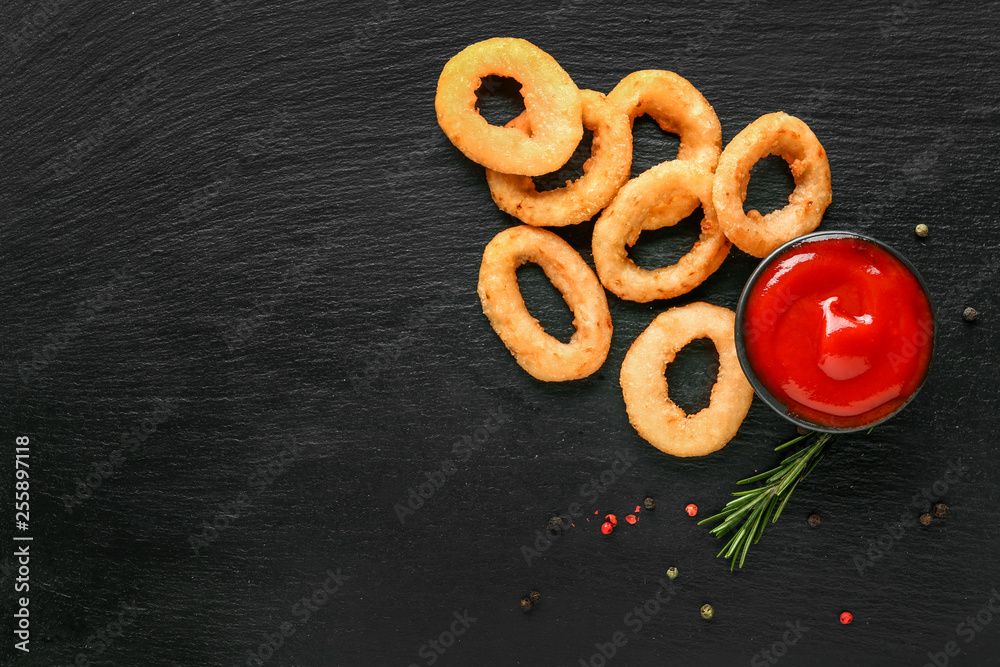 Tasty onion rings and tomato sauce on dark background