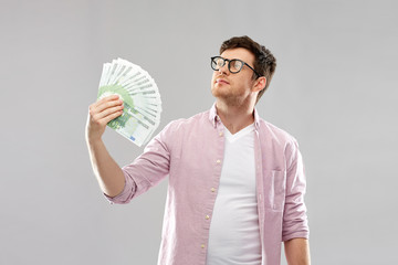 Wall Mural - money, finance, business and people concept - proud young man in glasses with fan of one hundred euro bank notes over grey background