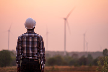 african engineer wearing white hard hat standing with digital tablet against wind turbine on sunny d