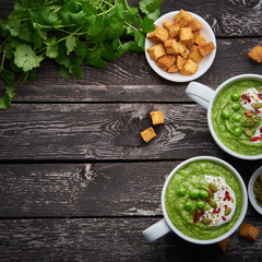 Wall Mural - Broccoli cream soup, vegetable green puree in two large white cup. Diet vegan soup of broccoli, zucchini, green peas on dark wooden background, top view, copy space.