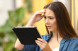 © Antonioguillem - Worried woman checking tablet content in the street
