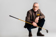trendy mature man in glasses holding golf club and while sitting on grey
