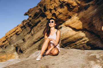 Wall Mural - Pretty long hair brunette tourist girl relaxing on the stones near sea.