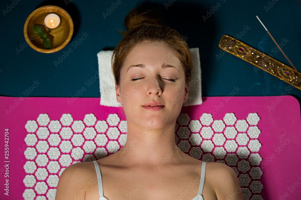 Woman with closed eyes Relaxing at home, lying on acupuncture mat. Candles and incense aroma sticks. - obrazy, fototapety, plakaty 
