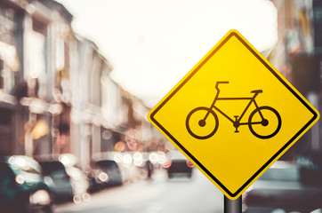 Wall Mural - Bicycle warning sign on blur traffic road with colorful bokeh light abstract background.