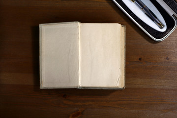 Fototapete - An open old retro book with white blank empty pages next to pen on which the designer can write a greeting text or a postcard on the wooden background of the library atmosphere