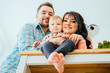 © Iryna - A low-angle view portrait of young happy family with a barefoot toddler girl sitting at kitchen table New home, happy healthy relationship concept.