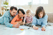 © Iryna - Charming family of four: father, mother, son, daughter drawing together, lying on the floor in a beroom. New home, happy healthy relationship concept.