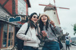 © PR Image Factory - two asian women travel in copenhagen denmark lifestyle in spring season. girls backpackers with hat standing on street city with windmill in background outdoor. female tourist point holding cellphone