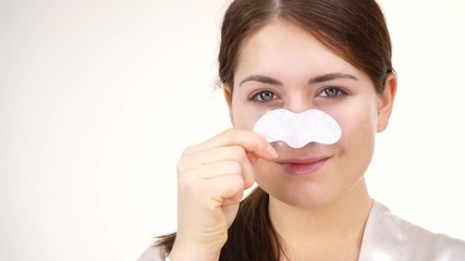 Poster - Woman appying clear-up strips on nose, using pore cleansing textile mask, against white. Girl taking care of skin complexion. Beauty treatment. Skincare