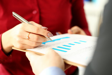 Female arm with silver pen give financial graph papers to client