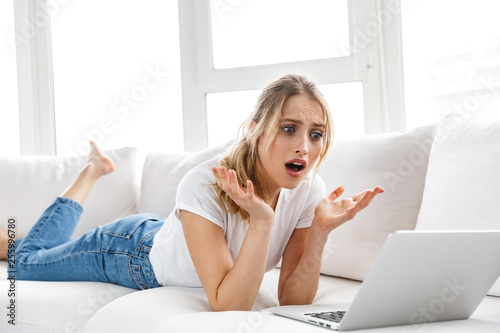 Photographie Portrait of outraged girl 20s using laptop while lying on couch in bright room a