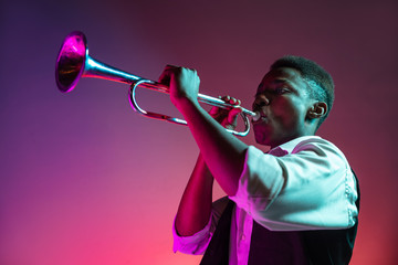 African American handsome jazz musician playing trumpet in the studio on a neon background. Music concept. Young joyful attractive guy improvising. Close-up retro portrait.