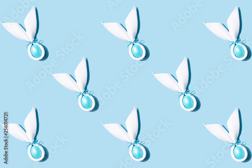 Pattern made of Easter bunny ears made of white napkin with egg on blue backg...