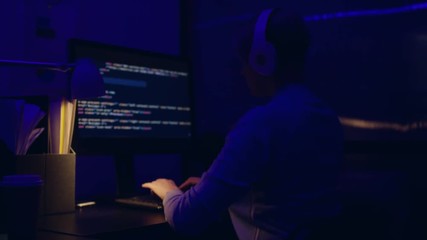 Tired frustrated business executive programmer is sitting late at night in the office, he is staring at the computer screen and receiving an error message. He wears earphones.