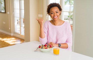 Young african american woman having healthy breakfast in the morning at home smiling with happy face looking and pointing to the side with thumb up.