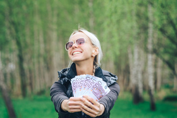 Wall Mural - An attractive young girl with a satisfied expression boasts of his pile of bills from European Euros, walking in a green Park.