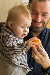 father plays with his one-year-old son at home and shows him a fruit