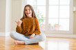 © Krakenimages.com - Beautiful young girl kid sitting on the floor at home smiling with happy face looking and pointing to the side with thumb up.