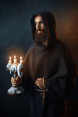 Wall Mural - Medieval monk in robe holds a candlestick in hands