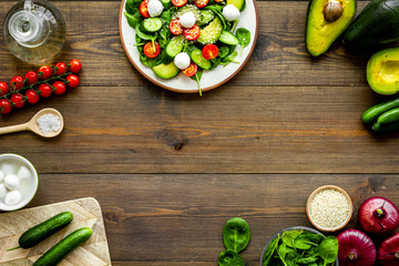 Wall Mural - Cooking fresh salad. Vegetables, greens, spices, plate of salad on dark wooden kitchen desk top view copy space