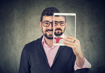 Cheerful man holding a tablet with serious self portrait on screen