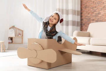 Poster - Cute little girl playing with cardboard airplane in living room