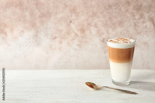 Photographie Glass of caramel macchiato on table against color background