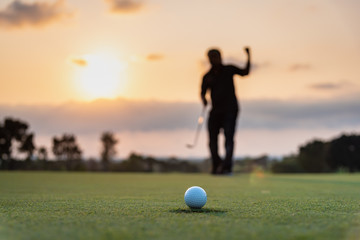 Wall Mural - Silhouette golfer showing happiness when win in game , white golf ball on green grass of golf course with blur background.