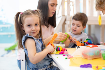 Wall Mural - Teacher teaches kids modeling clay in playroom at daycare or kindergarten