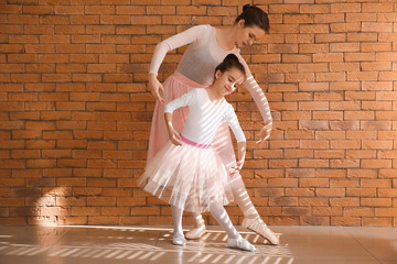 Little ballerina training with coach near brick wall