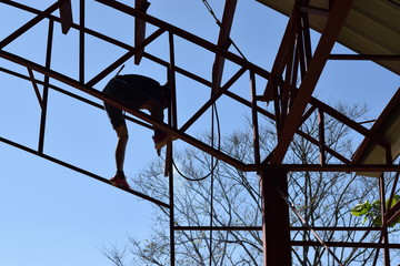 Steel worker welding trusses of a covered gym court. silhouettes