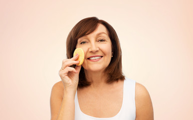 Sticker - beauty, skin care and old people concept - smiling senior woman cleaning her face with exfoliating sponge over beige background