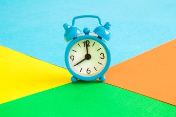 Close up of small blue alarm clock on multicolored background abstract.