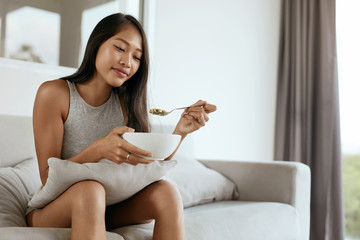 Smiling woman eating healthy breakfast at home in morning