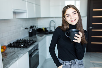 Wall Mural - Beautiful happy young woman drinking morning coffee in the kitchen at home