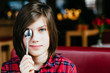 © Iryna - Close up portrait of teenager boy covering eye with spoondrinking tea sitting on red couch having breakfast in cafe interior.