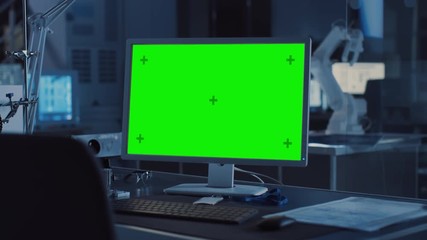 Poster -  On the Desk Computer with Isolated Green Mock-up Screen Display. In the Background Robot Arm Concept Standing in Heavy the Dark.Industry Engineering Facility