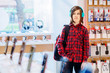 © Iryna - Stylish casual hipster teenager boy at plaid red shirt, backpack using new headphones at electronics store.