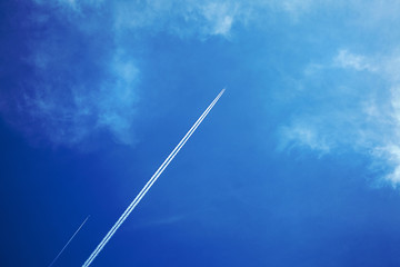 Two planes in the blue sky with white clouds. The aircraft leaves traces