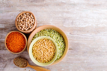 Canvas Print - Different beans in bowls on a white wooden table, top view