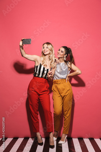 Fototapeta na drzwi i meble Zdjęcie dwóch eleganckich dziewczyn z lat 20. w stylowym stroju, trzymając smartfon i robiąc selfie