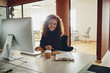 © Flamingo Images - Smiling businesswoman sitting at her workstation in a large offi