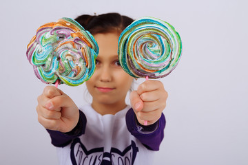 A girl holds in two hands multicolored candies on a stick, showing them to the camera. sweet life