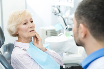 Senior woman suffering from toothache visiting dentist