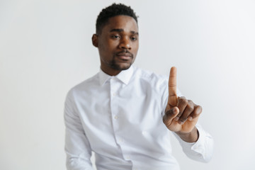 Handsome businessman pointing his finger to the camera and slicking virtual image or text, finger is in focus while his face is out of focus. Shallow depth of field. Young african american guy