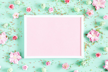 Wall Mural - Easter decor, composition. Blank photo frame, flowers, easter eggs on pastel mint background. Flat lay, top view, copy space